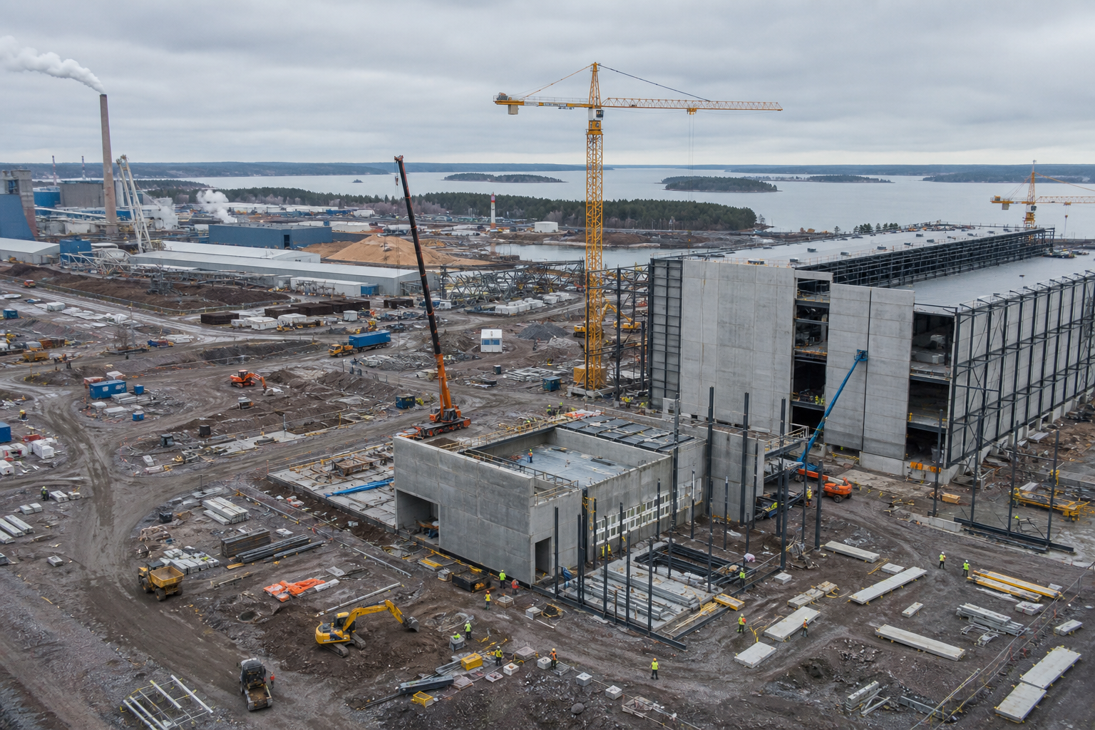 Ilmakuva Kotkan akkumateriaalitehtaan rakennustyömaalta. Nostureita ja keskeneräisiä tehdasrakennuksia, työntekijöitä turvavarusteissa.